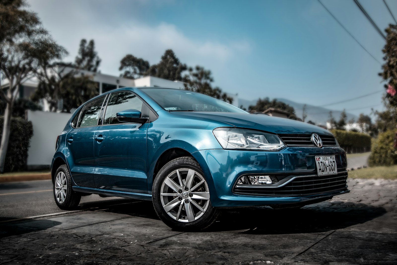 A blue Volkswagen hatchback on a tropical street